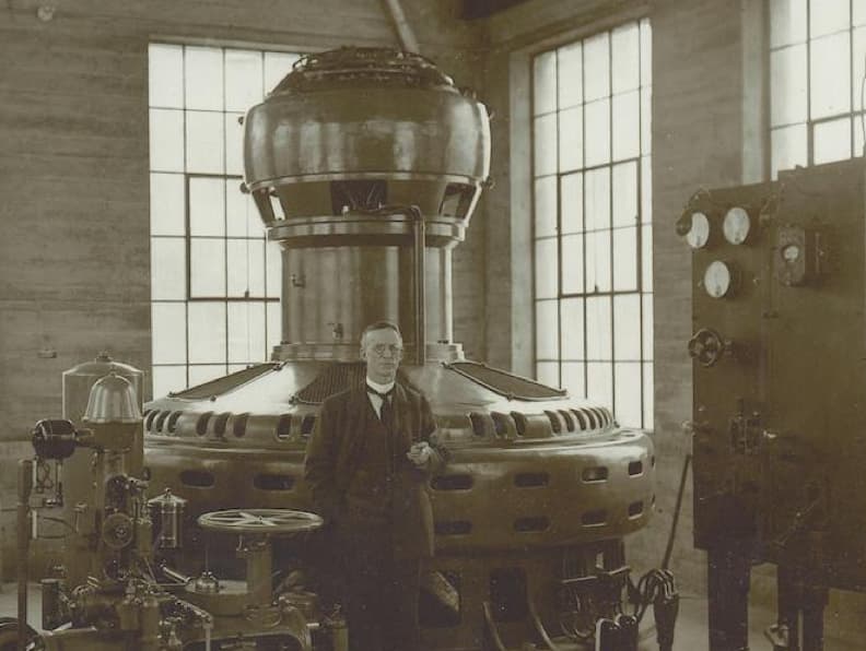 Photographie en noir et blanc d’un homme dans une grande pièce avec des machines.